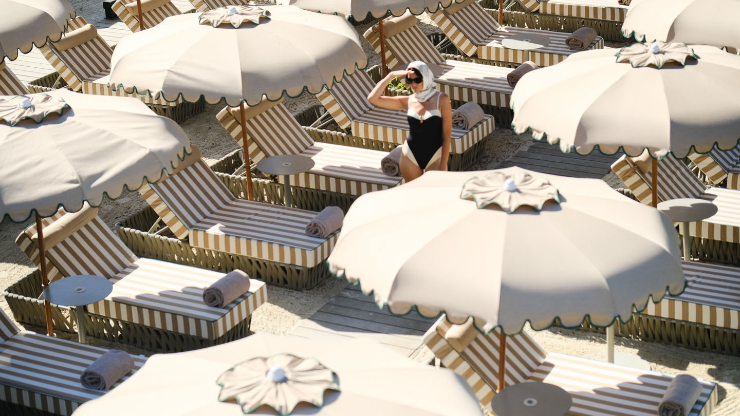 Parasol sur la plage privée du Beau-Rivage Palace Lausanne avec femme cherchant une place transats élégants et ambiance estivale dans un hôtel de luxe à Lausanne et palace 5 étoiles