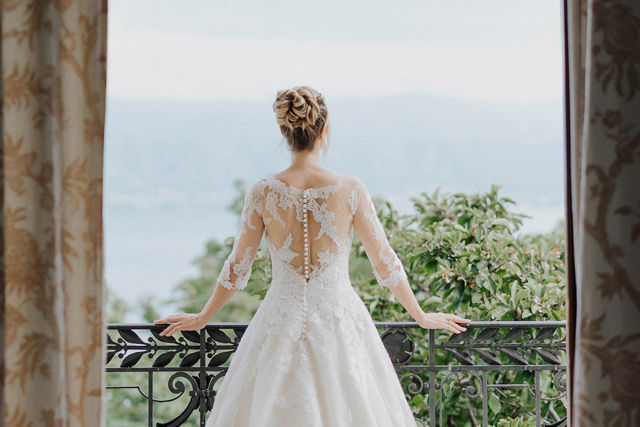Mariée en robe blanche photographiée devant une grande fenêtre du Beau-Rivage Palace Lausanne, portrait élégant dans un cadre architectural historique et romantique, de dos et regardant le parc et la vue sur le Léman